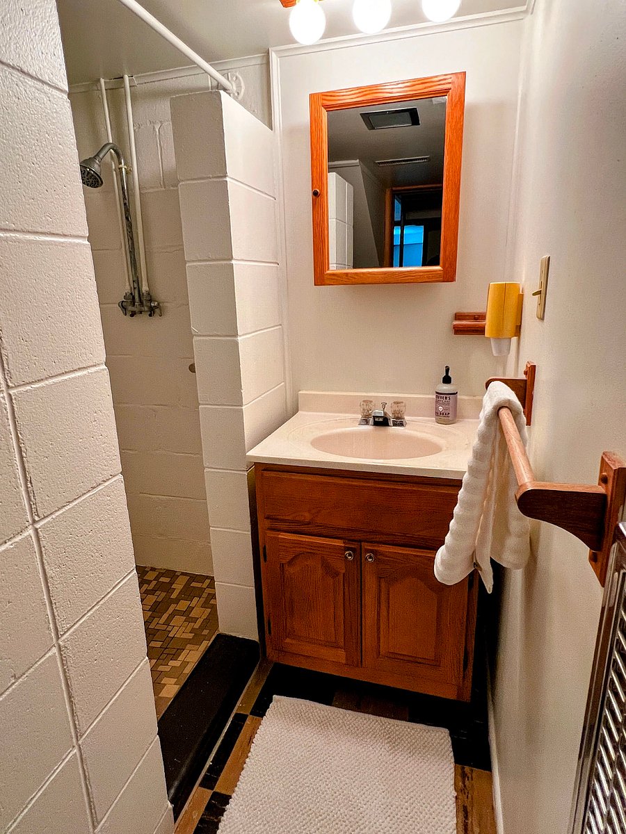 The bathroom has a sink, small storage space, and a shower.