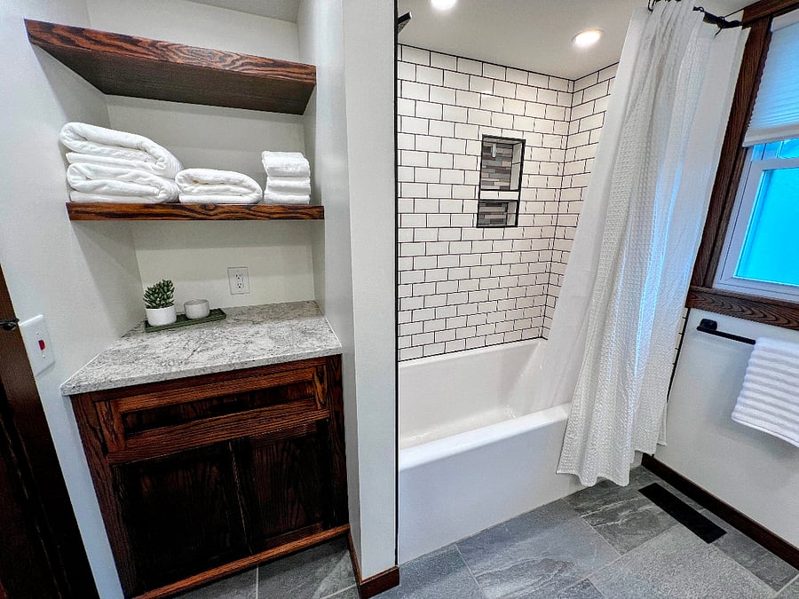 The shower is tiled and behind the door is additional shelf and cabinet storage. 