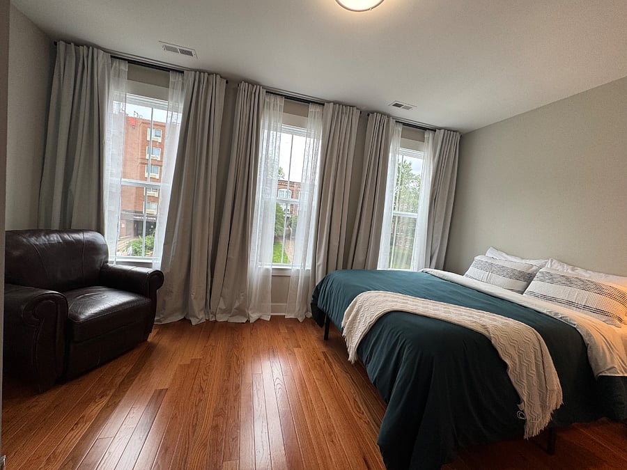 Bedroom B with lots of windows and a recliner chair in corner. Available now.