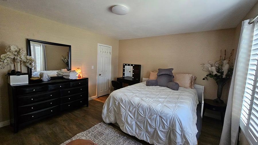 Envision a serene black-and-white room furnished with a comfortable bed, a walk-in closet, a vanity, a dresser, and a television. It constitutes an ideal, tranquil, and pristine environment in which one may relax after a demanding day of work.