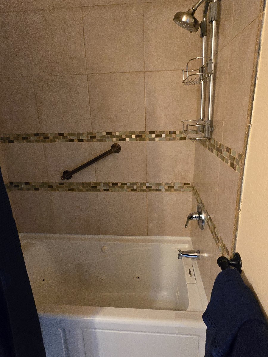 Warm light catches the mosaic tile of a quiet bathroom where a jetted tub sits ready for a relaxing soak or a shower. 