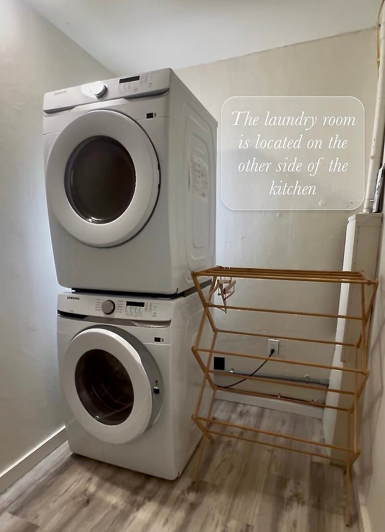 The laundry room is on the other side of the kitchen. Inside is a stacked washer & dryer, a drying rack and a table.