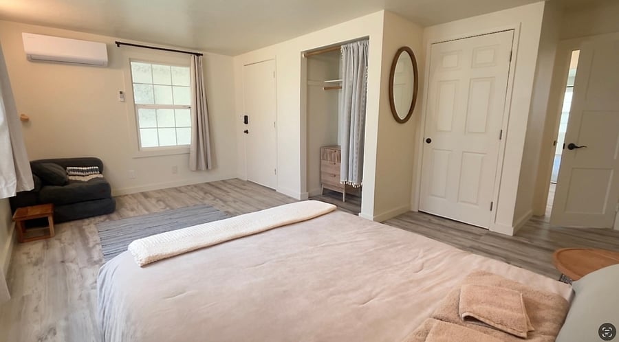 The second bedroom has a full-size bed, an average sized closet, a small dresser, and a comfortable corner chair. Reading lights are mounted above the bed & chair.
This bedroom, also, has three doors. One door connects the bedroom to the TV/living room, one connects to the bedroom and the third to the backyard.