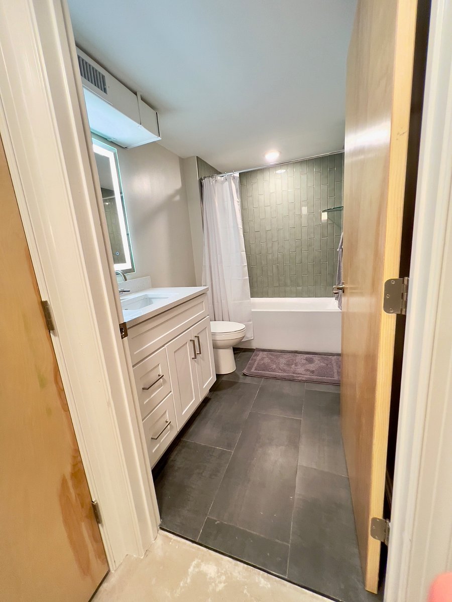 Spacious primary bathroom with beautiful tile on the floor and wall and lighted mirror.