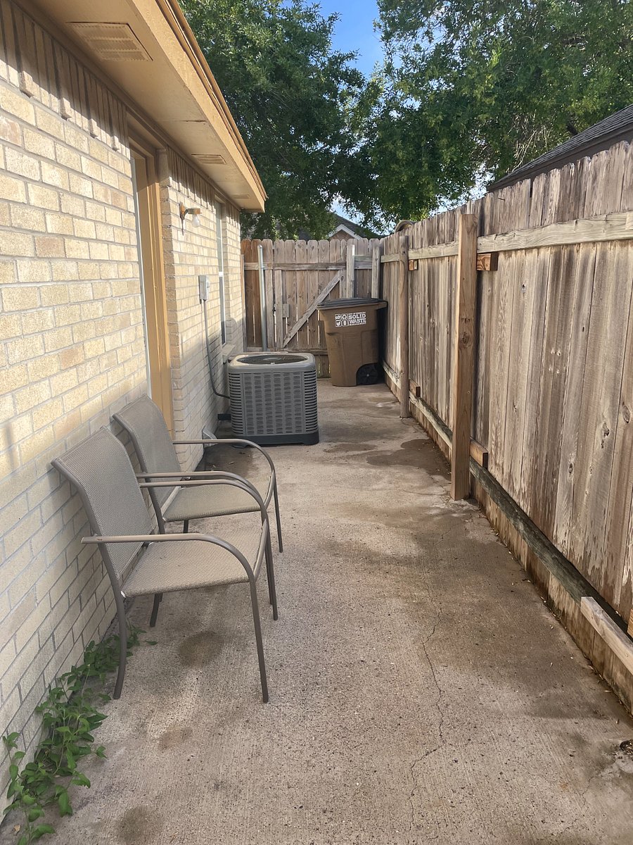 Enclosed patio with two chairs and table. Utility hangers on opposite wall with mop and outdoor broom.