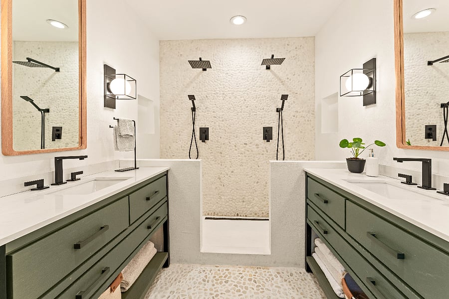 Primary bathroom featuring a walk in shower, dual showers, shaving bench, product nooks, matching vanities, and a stone floor and accent wall.