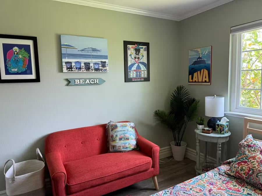 Downstairs queen bedroom: This inviting corner features a comfy loveseat with playful beach decor and soft natural light, creating a welcoming space to unwind, read, or enjoy quiet time during your stay.