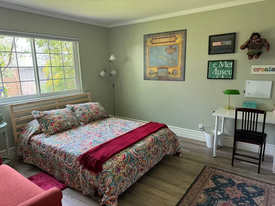 The downstairs bedroom features a queen bed with cozy, colorful bedding, plenty of natural light, a full-length window, and a writing deskperfect for relaxing or getting a little work done during your stay.