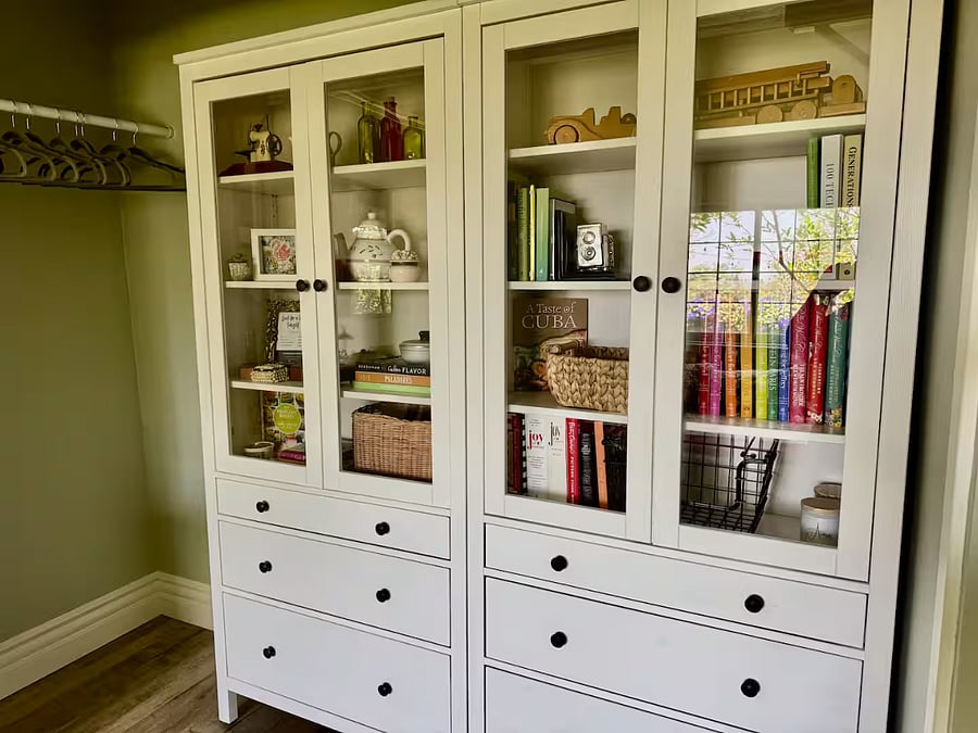 Downstairs bedroom includes elegant storage with drawers and shelves stocked with books and decor. Hanging space and baskets make it easy to settle in and stay organized.