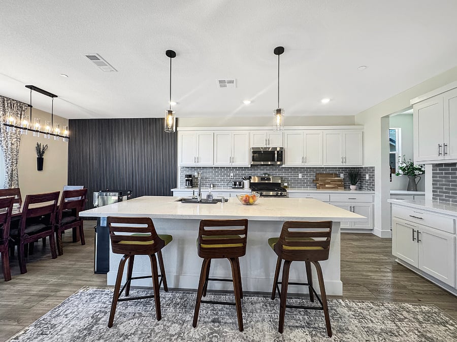 Huge kitchen island with three modern decorative chairs and gorgeous lighting.