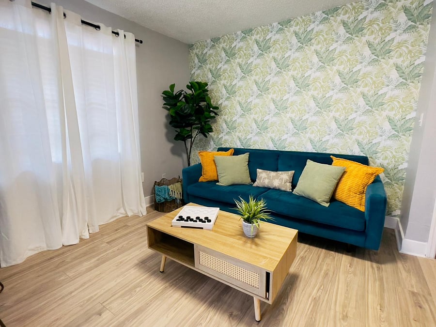 Bright and inviting living room with tropical wallpaper, a teal velvet sofa, and vibrant accents for a modern Cuban vibe.