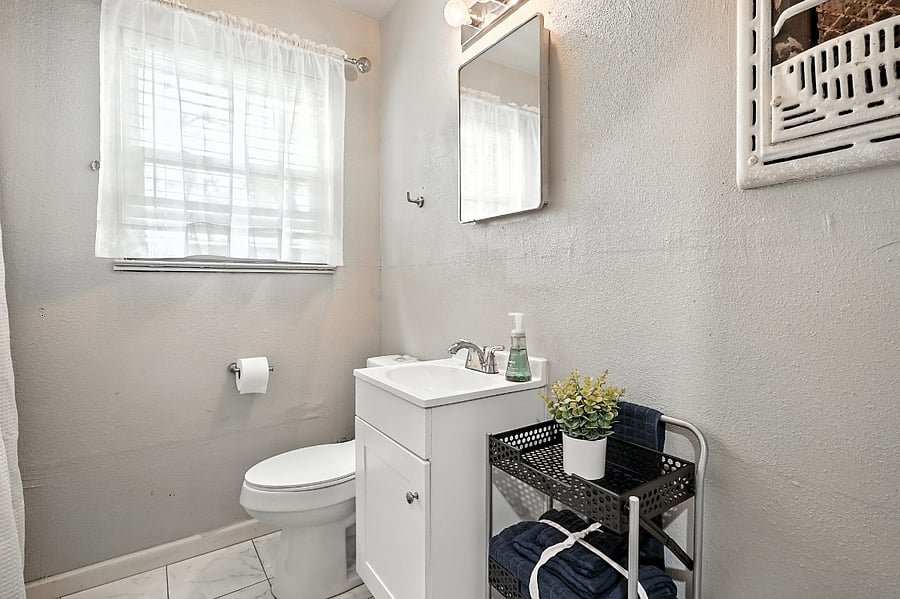 Bathroom with ceramic tile, extra towels, cabinet mirror, cleaning supplies and rolling rack for storage