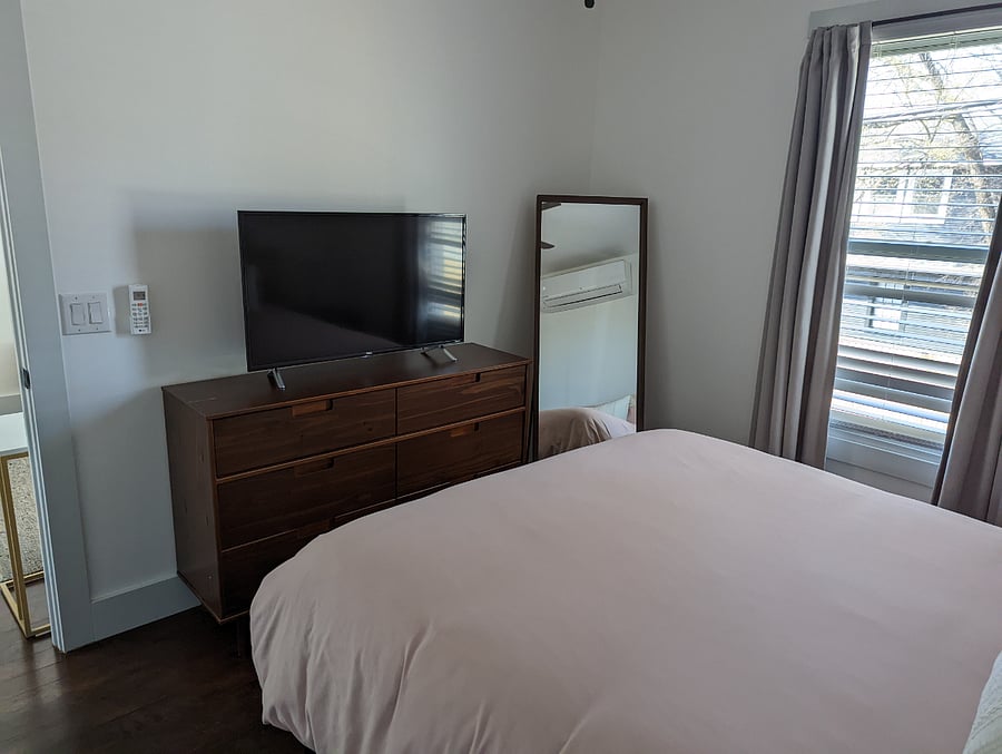 Bedroom with queen bed, smart TV, and full-length mirror.