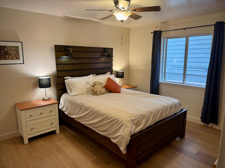 Second bedroom, with queen bed, dresser, and nightstands. All bedrooms have ceiling fans, blackout curtains, portable fans, and closets. This bedroom has a private bathroom (see photos) and a sliding glass door leading to a fenced in yard with a patio including chairs and a small table.