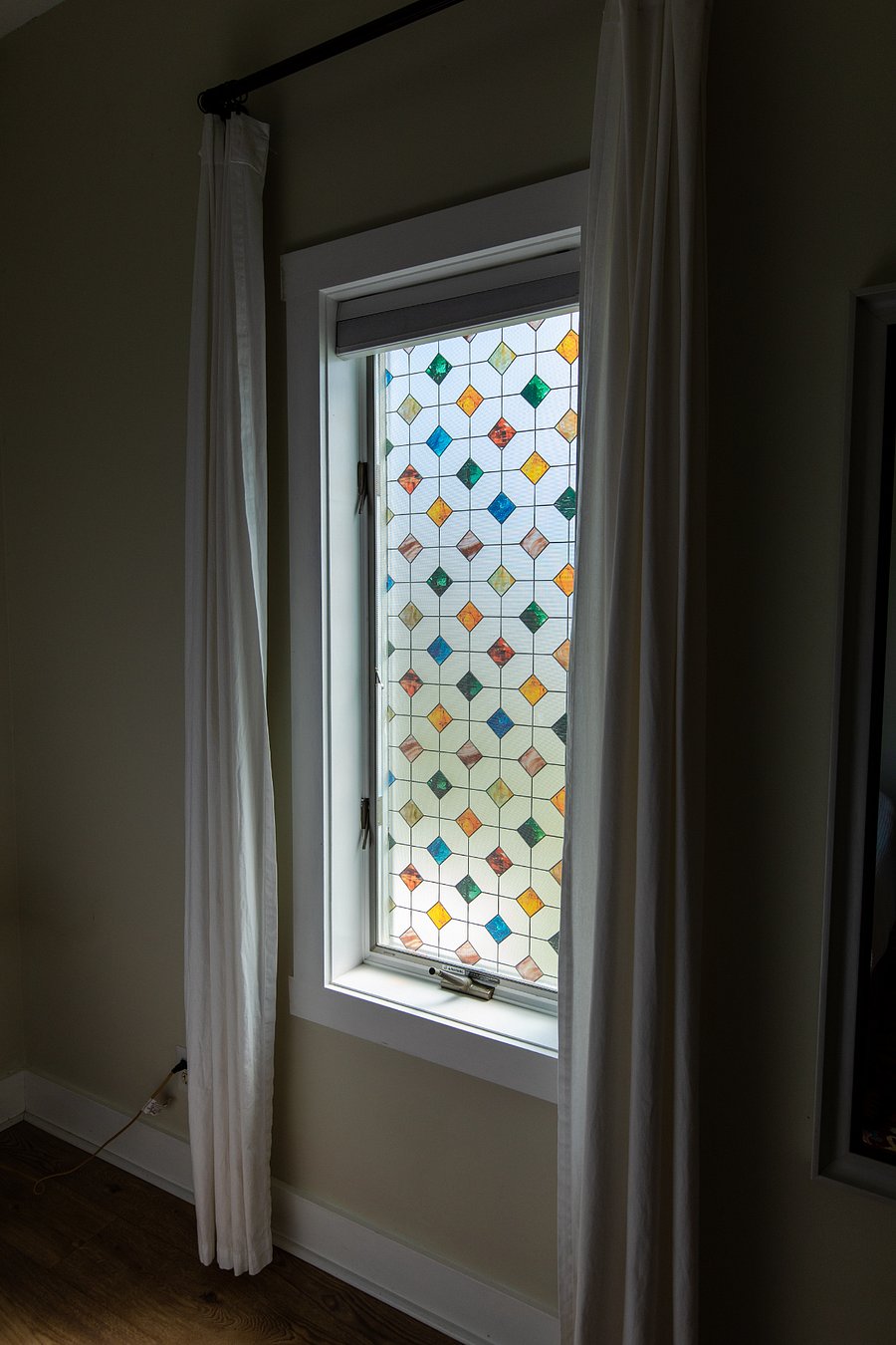The bedroom window with its cheery stained glass finish adds joy and provides privacy. The window treatment consists of blackout shades and light-filtering curtains.