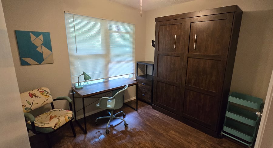 Office and guest room. The desk looks out to the street through greenery and the cabinet holds a full-size bed.
