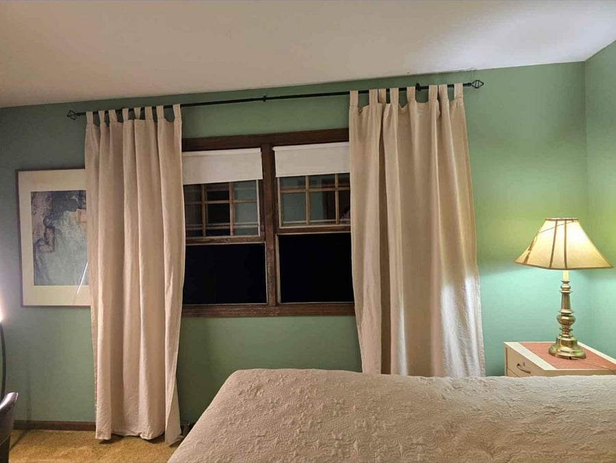 A cozy bedroom with a large window, thick curtains for privacy, and a bedside lamp for comfortable evening reading.