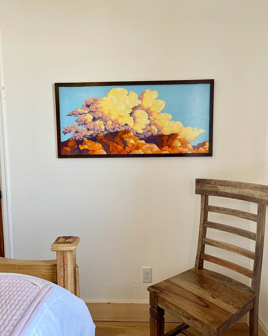 A painting featuring fluffy clouds and distinct landscape in the downstairs bedroom with the queen size bed