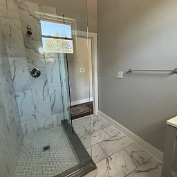 Shared bathroom featuring a glass-enclosed walk-in shower with marble-style tiling.