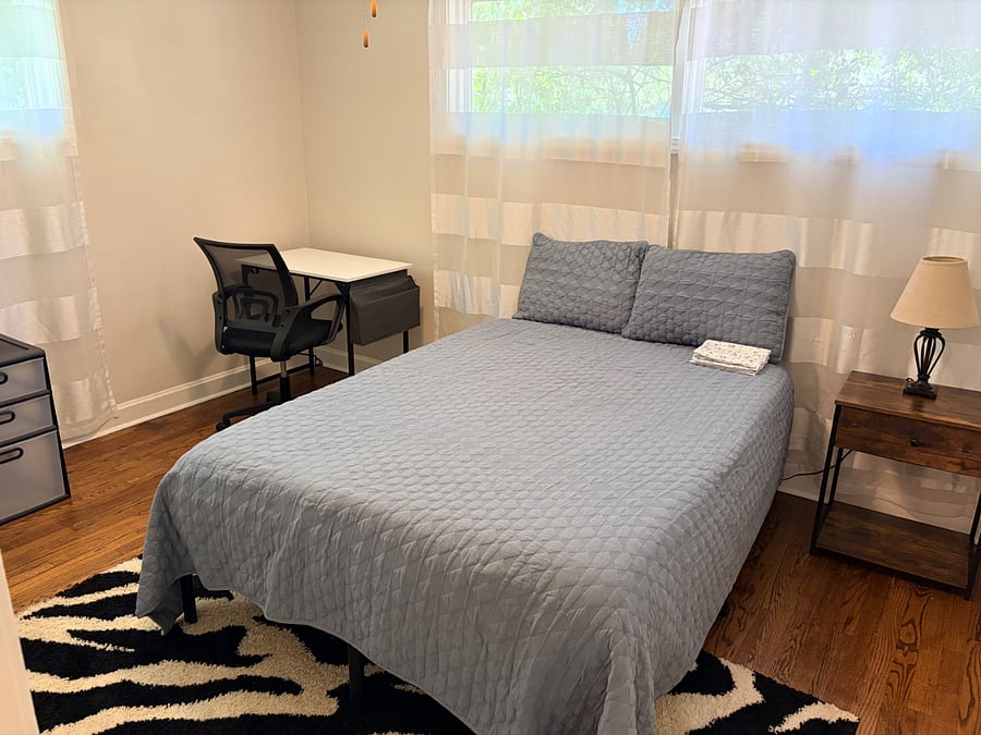 Bedroom with full sized bed, desk, chair, nightstand, rug, lamp, drawers, and 2 large sets of storage drawers in the closet along with storage basket