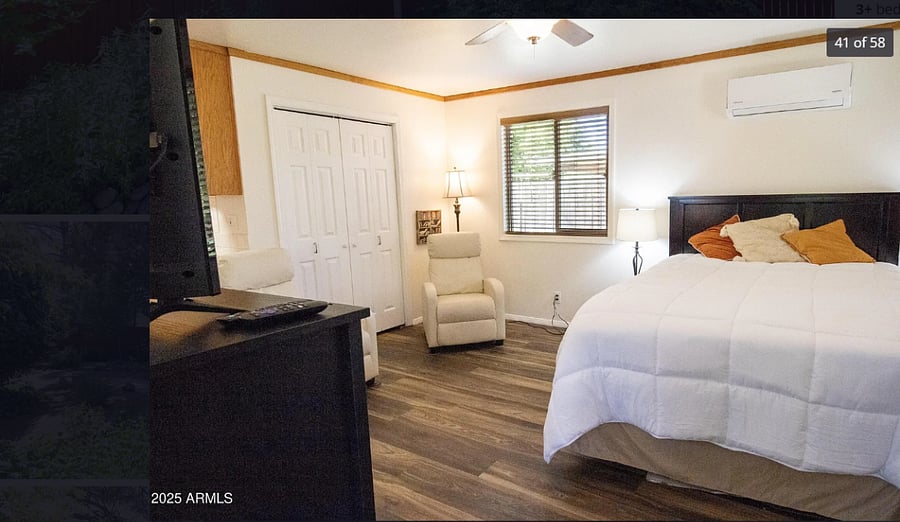 Studio view upon entry with queen bed and lounge chairs, mini split above the bed and ceiling fan. 