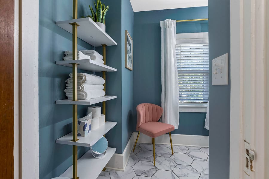 The bathroom is spacious and includes shelving for towels and toiletries, as well as a seat