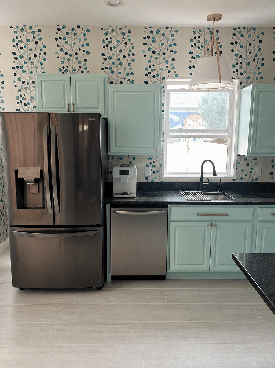 Cheerful, light-filled kitchen with mint cabinetry, stainless-steel appliances, dramatic botanical wallpaper, generous storage, and a deep sink beneath the window.