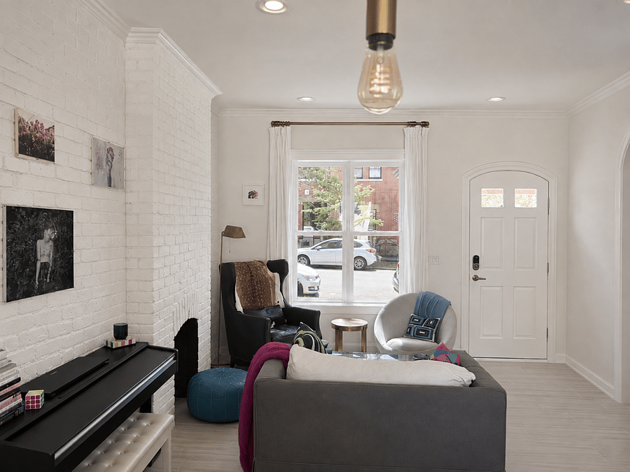 Sun-filled living room with original painted brick, oversized windows, multiple seating areas, and a warm, eclectic mix of vintage and contemporary details.