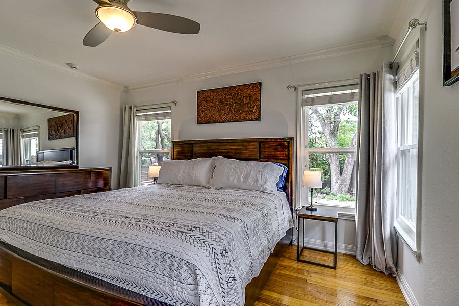 View of master bedroom with king bed, fan, nightstands, dresser and closet. Windows overlook the backyard.