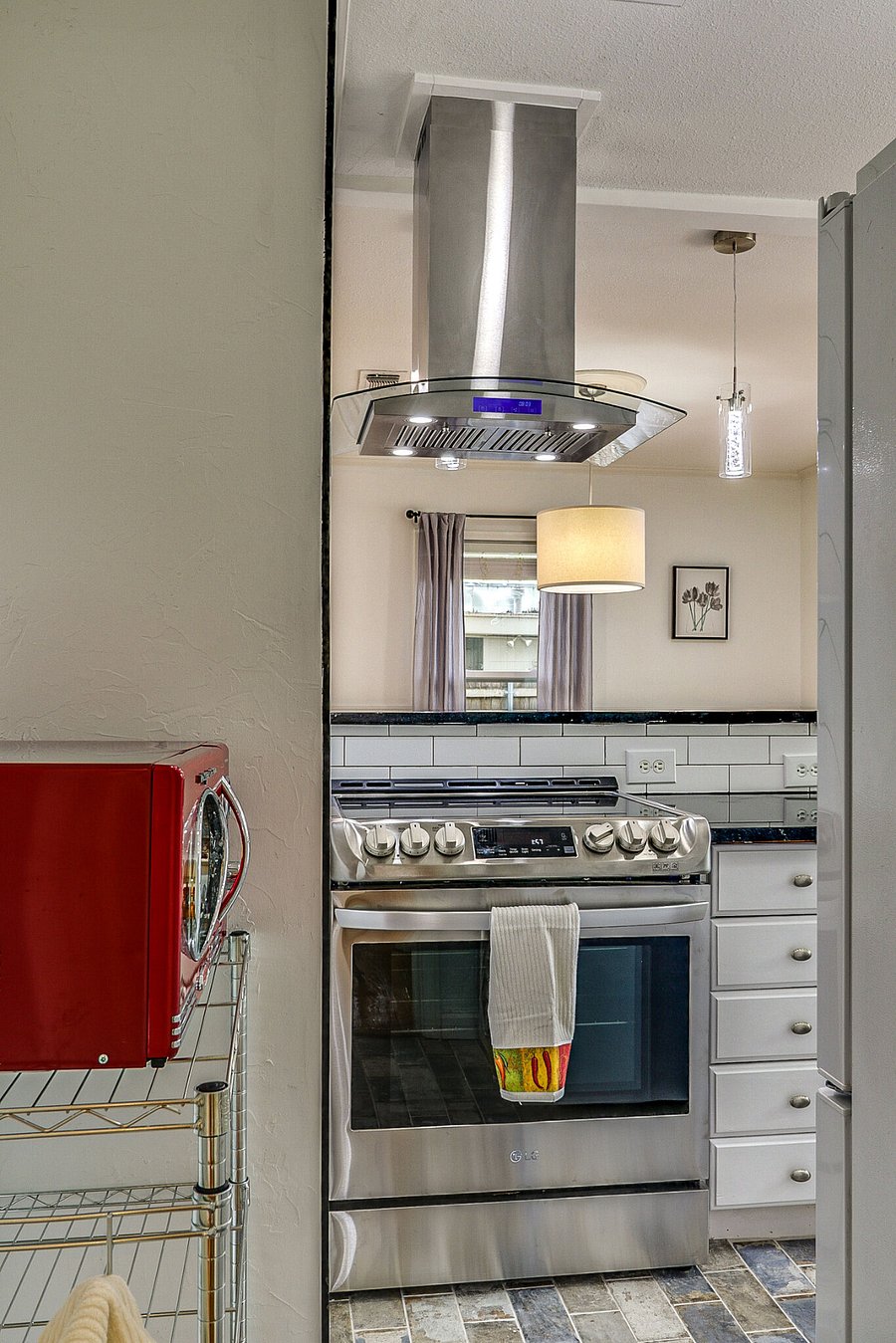View from kitchen over stove/oven into dining area with four chairs and table plus bar seating for two