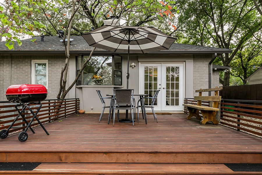 Raised deck just off the ground level with grill and dining with umbrella. Also large canopy tree overhead provides shade.