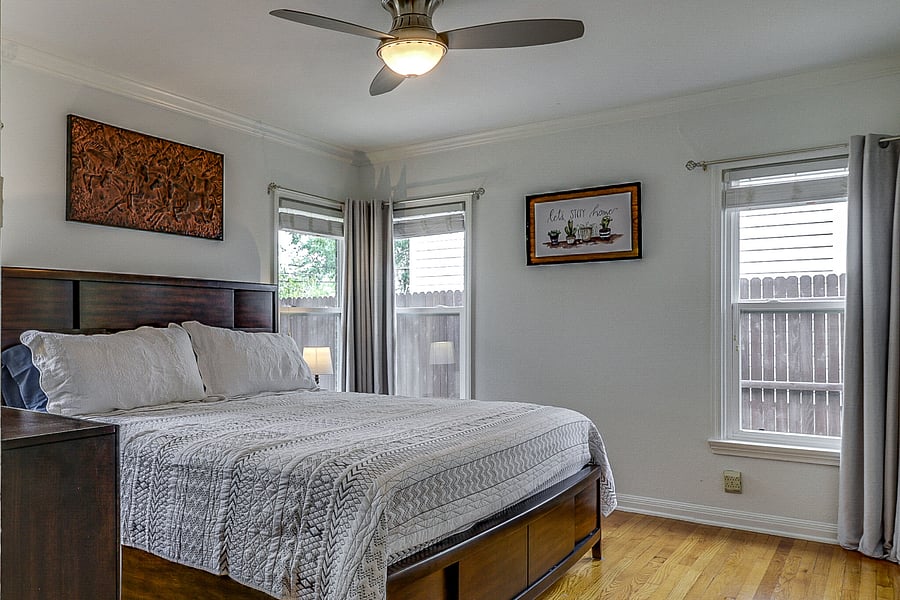 View of master bedroom with king bed, fan, nightstands, dresser and closet. Blackout curtains on all bedroom windows