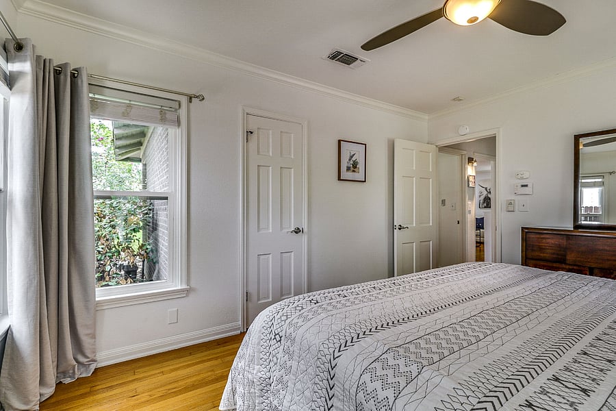 View of master bedroom with king bed, fan, nightstands, dresser and closet. Windows to right side and backyard have blackout drapes and blinds
