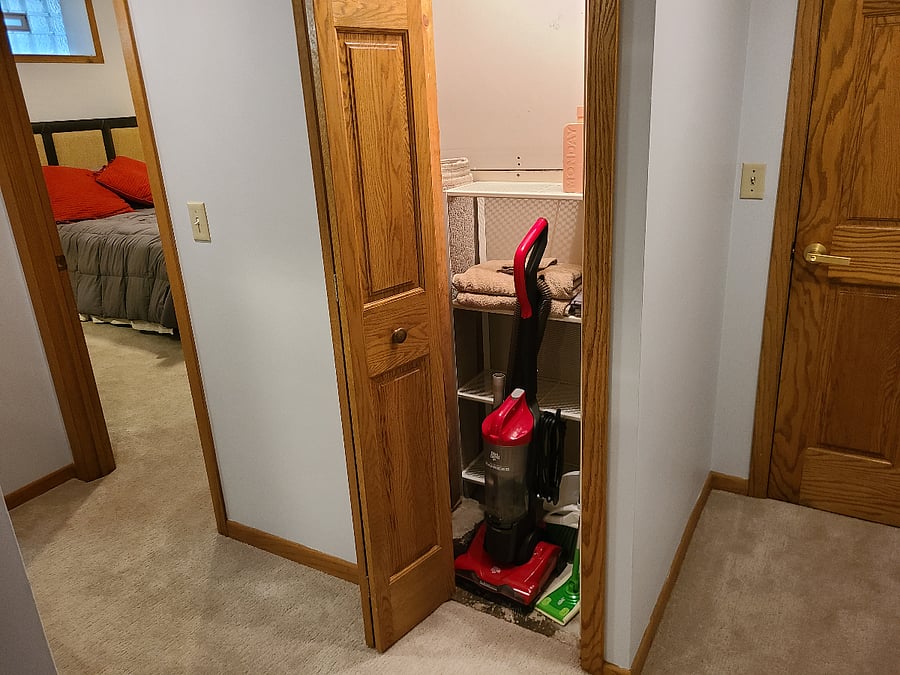Hallway storage closet with bedroom door on the left and access to laundry at right.