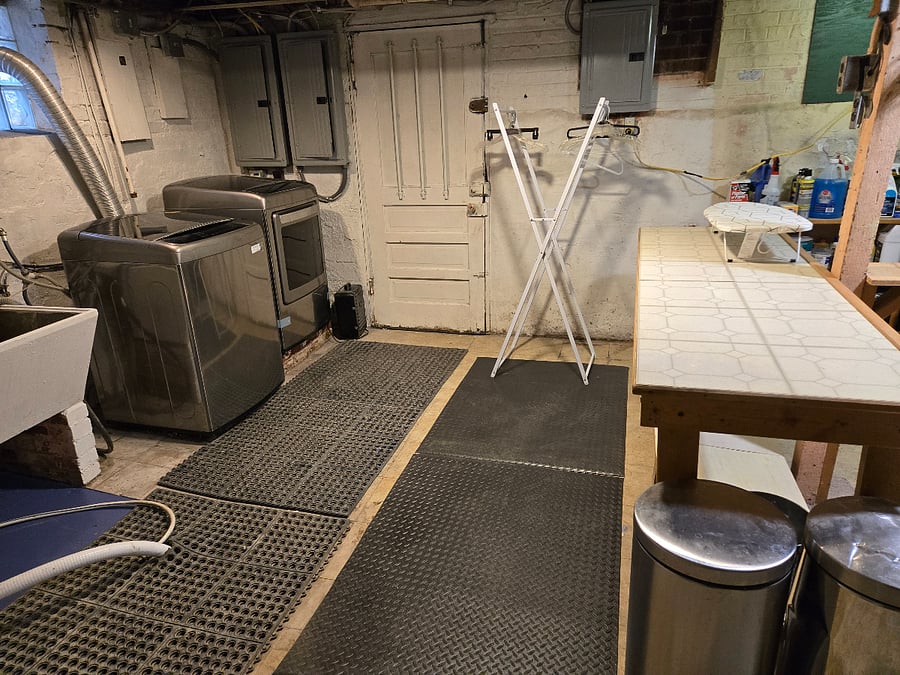 Laundry room in basement has good lighting, modern washer and dryer, folding table, hanging rack, and ironing board. There is an adjoining half-bath.