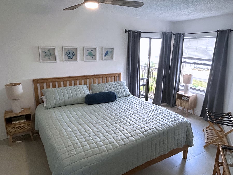 Bedroom 2 features a king-sized bed, beachfront views, a roomy closet, a TV, a ceiling fan and access to the balcony. 