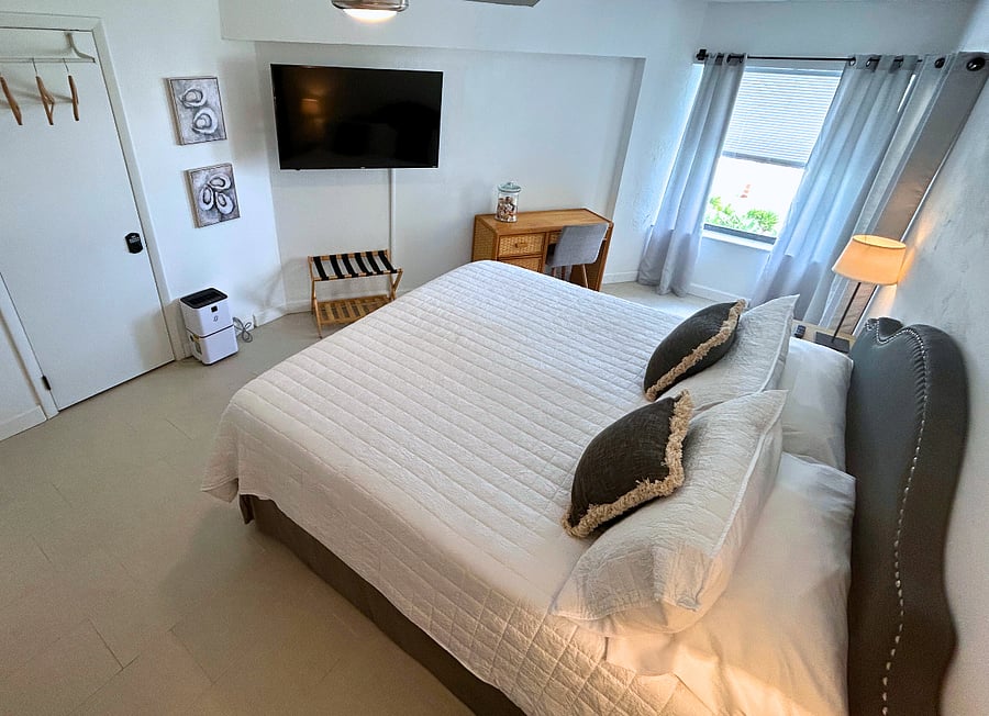 Bedroom 1 features a king-sized bed, beachfront views, a TV, a ceiling fan, a desk,  and access to the balcony. 