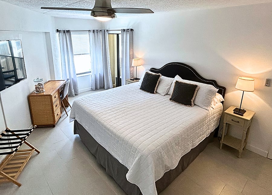 Bedroom 1 features a king-sized bed, beachfront views, a TV, a ceiling fan, a desk,  and access to the balcony. 