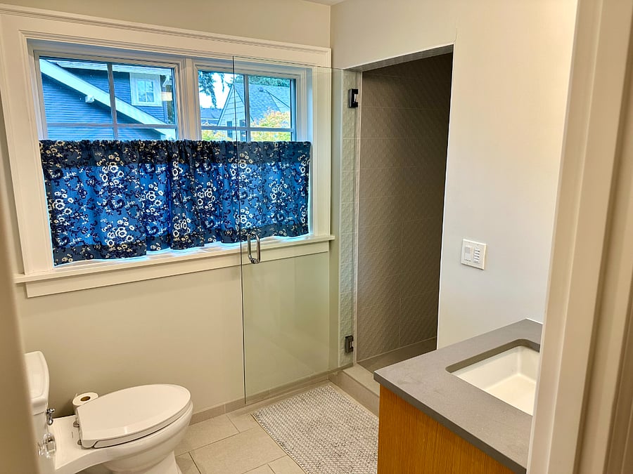 Bathroom with two large windows for natural light, sink, and walk-in shower with full tiles from celing to floor.
