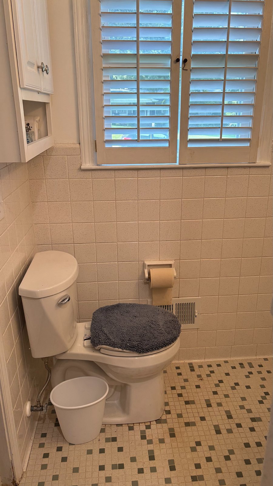 Toilet, trashcan, window, and cupboard to store toiletries