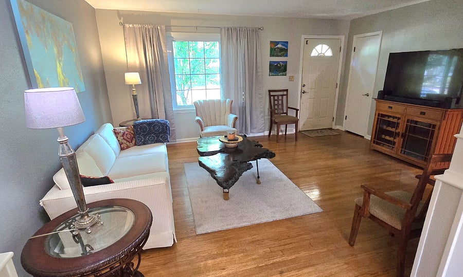 Bright living room with 55" smart TV, cozy seating, and natural light from the front window.