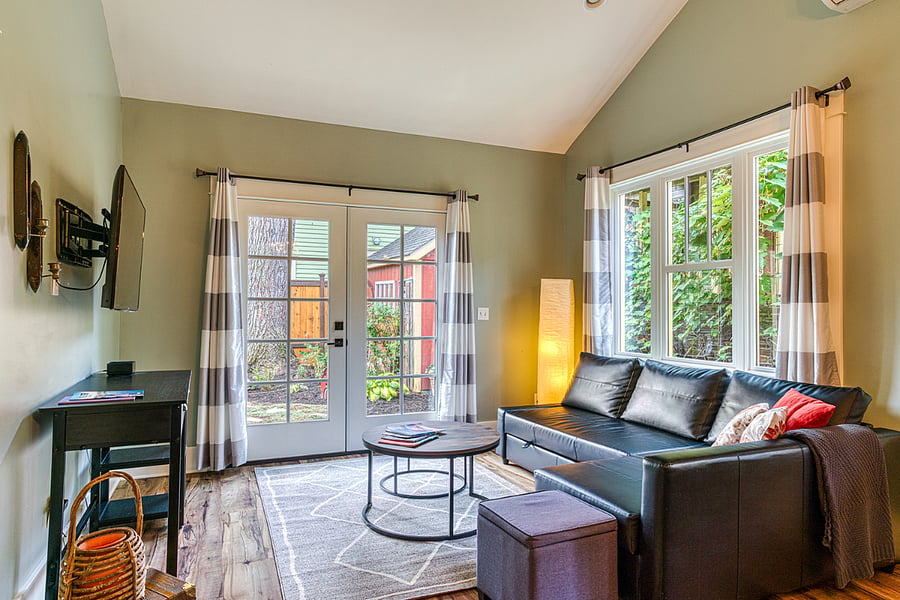 A cozy living room with a TV offering streaming apps, opens through French doors to stunning natural beauty, with grapevines and trees surrounding the space, creating a peaceful retreat.