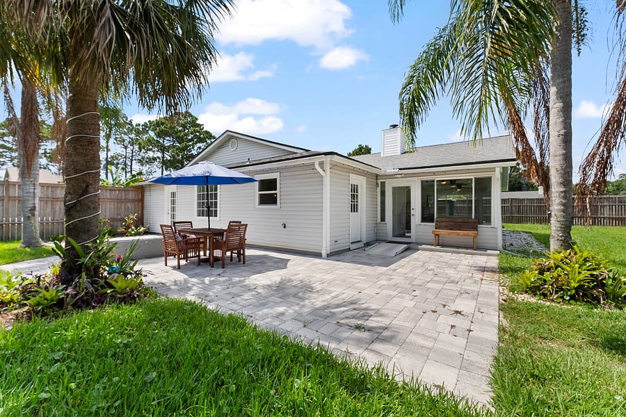Lush green yard, natural wood bench, and acacia dining set under an umbrella. A serene, classic Florida settingperfect for relaxing, dining, or simply enjoying the peace and calm.