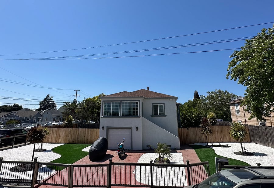 The duplex sits on a large corner lot. The entrance to the lower unit is on the right side, through the wooden gate.