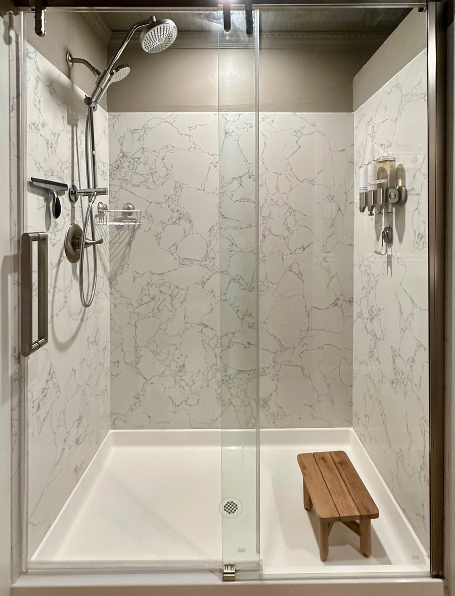 Full-size shower with a rainhead and wand. Shampoo, Conditioner, and Body wash on the wall.