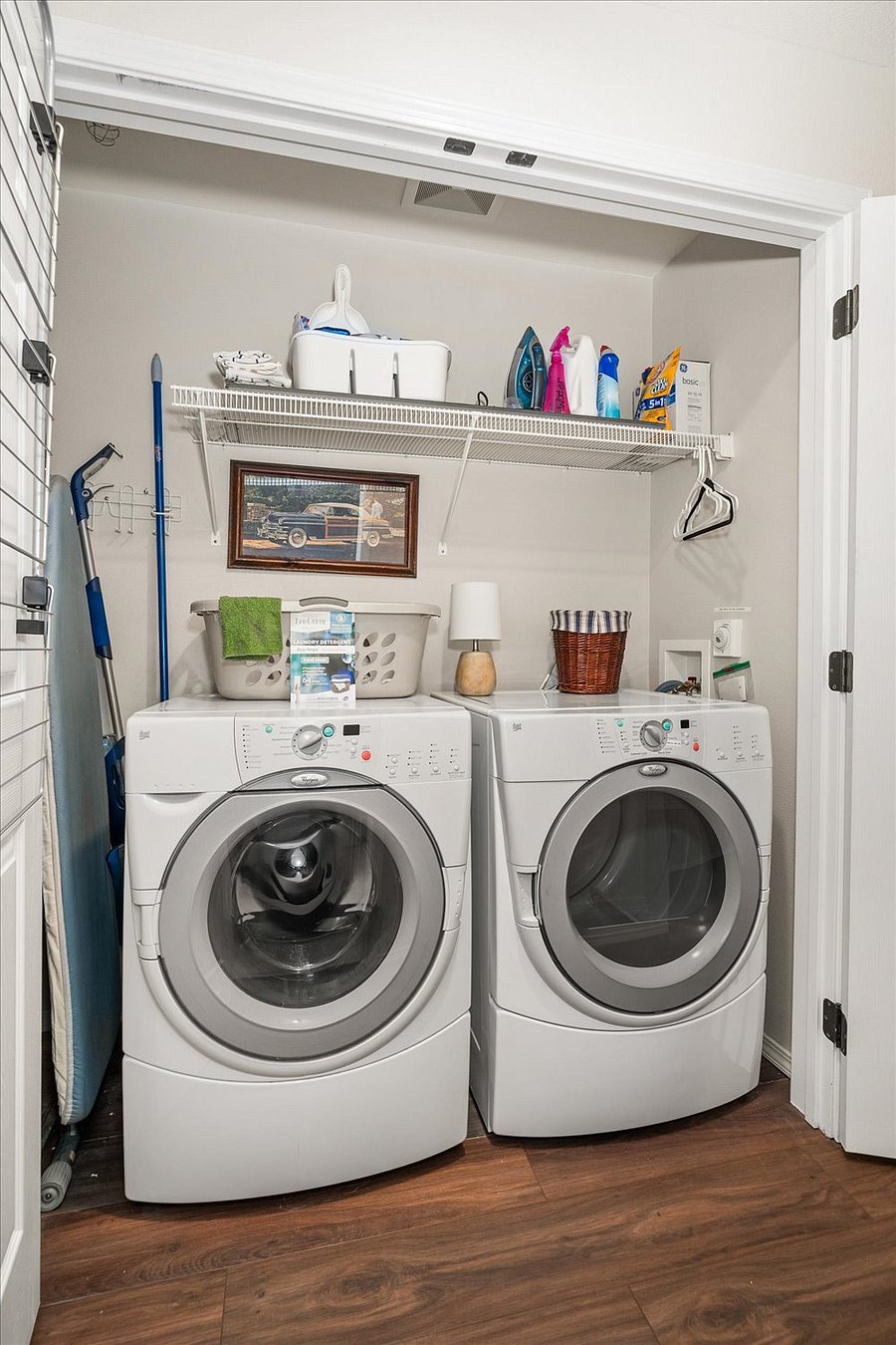 Washer and Dryer with ironing board, detergent and cleaning supplies.