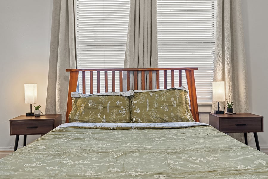REAR BEDROOM. Real wood queen bed with extremely comfortable mattress above a nice rug. Black out curtains. Wall art, and chest of drawers are shown in other pictures. Also not shown is a single seating chair in corner for reading and lounging.