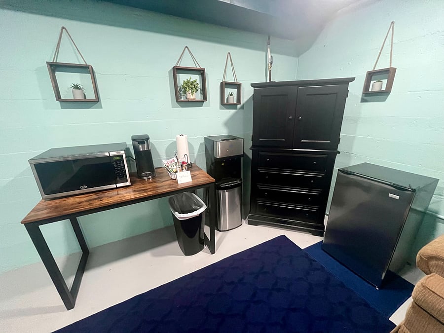The kitchenette area is equipped with a microwave, keurig coffee maker, hot/cold water dispenser, large minifridge, and cupboards with dishes, silverware, Tupperware and more.