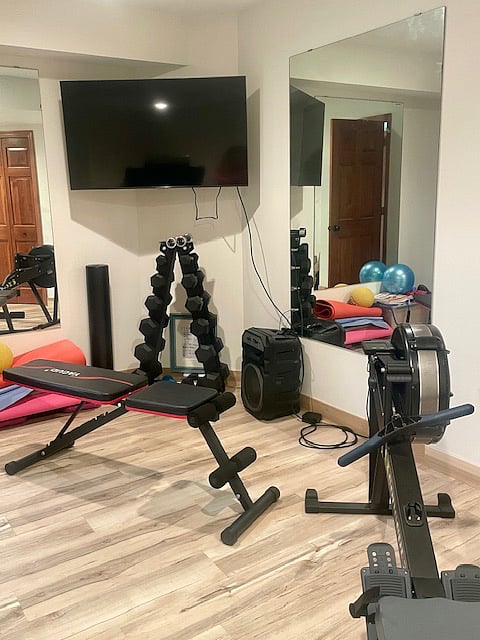 Home Gym with Smart TV, Weights, Treadmill, Rower, Bench, and Yoga Mats.