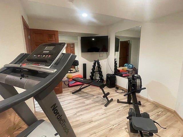 Home Gym with Smart TV, Weights, Treadmill, Rower, Bench, and Yoga Mats.